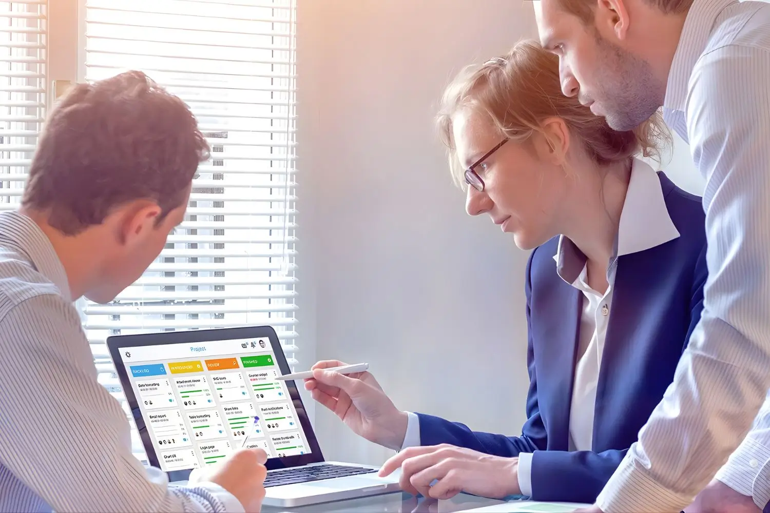 A professional business meeting in a modern office where a person in a suit is explaining a document to another individual with a laptop open.